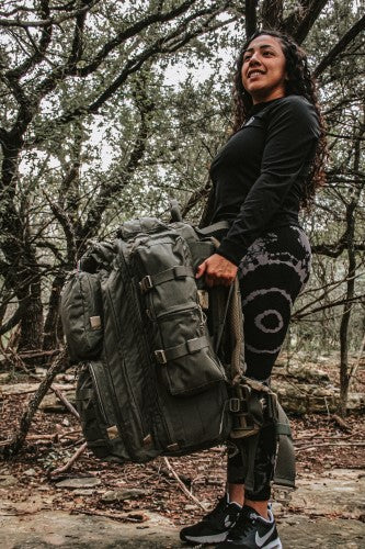 A woman confidently walking through a forest with a Grassman pack from Squatch Survival Gear, ready for any adventure or emergency. Her sturdy, American-made backpack 